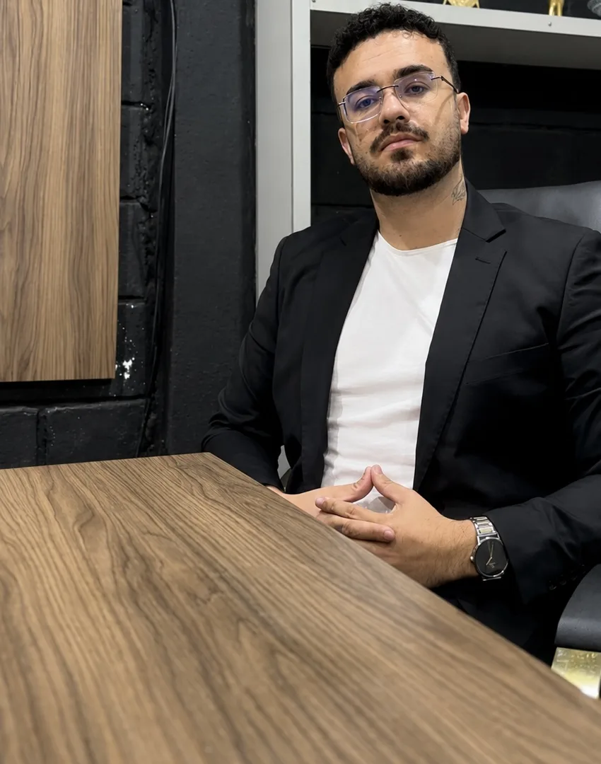 Lucas Oldmen sentado à mesa do escritório, de blazer preto